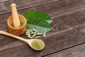 image of kratom powder on wooden spoon with capsules leaves and a mixing bowl