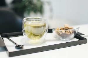 Image of green kratom tea in a glass next to peanuts on a serving tray